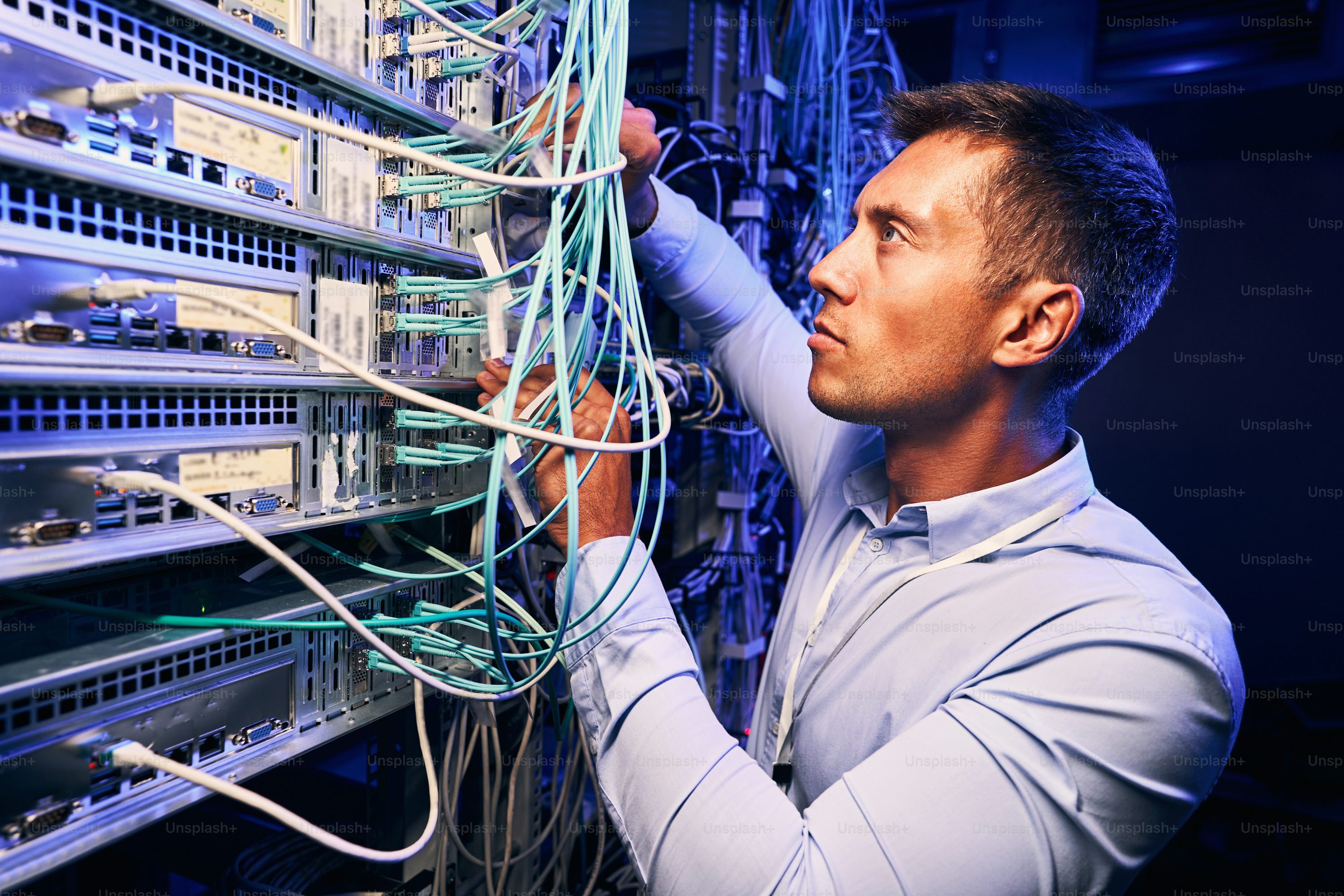 A technician inspecting fiber optic cables in a modern server room with rows of blinking hard drives