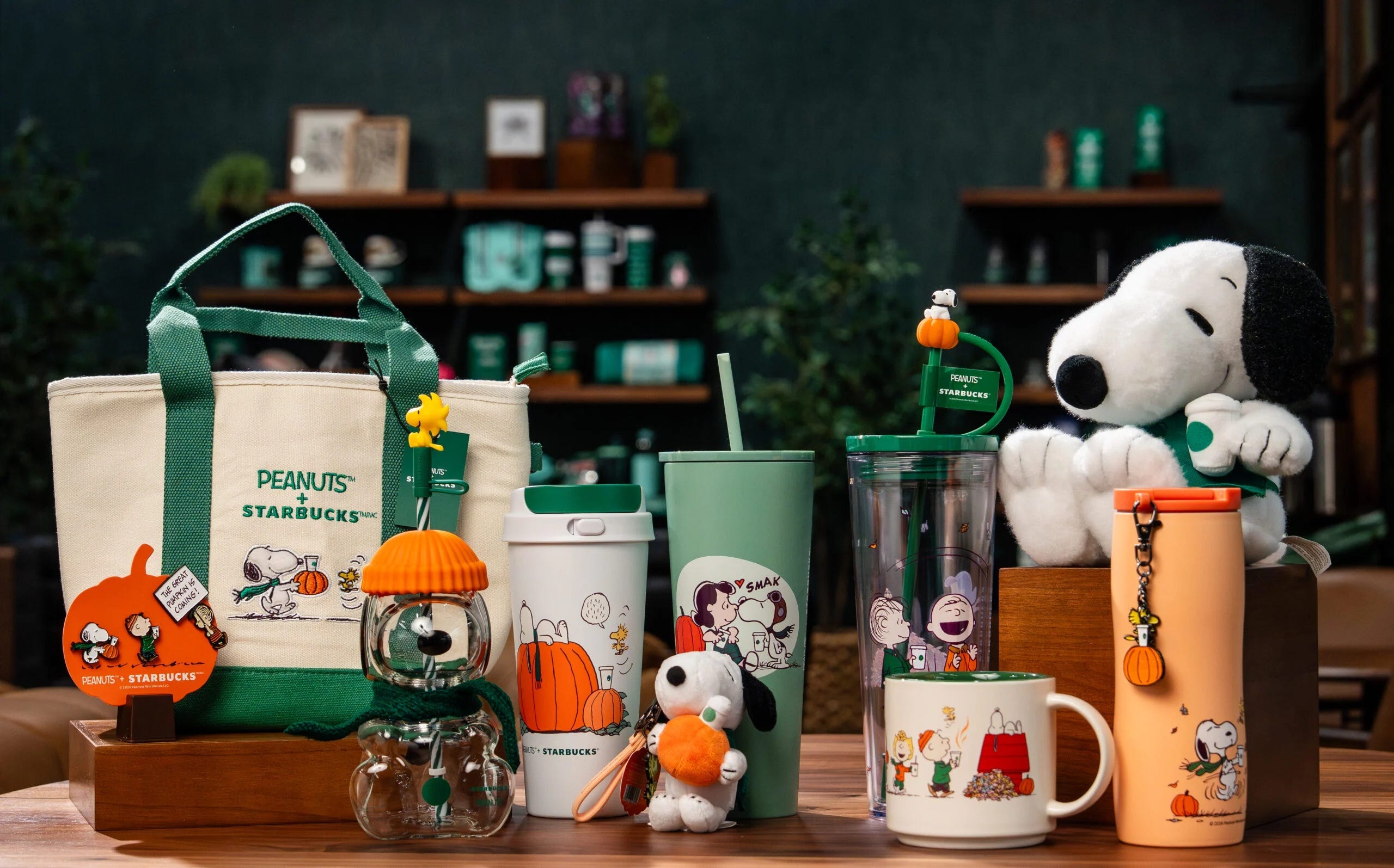 A close-up of a limited edition Snoopy-themed Starbucks cup sitting on a wooden table in a cozy cafe setting with latte art visible in the background.