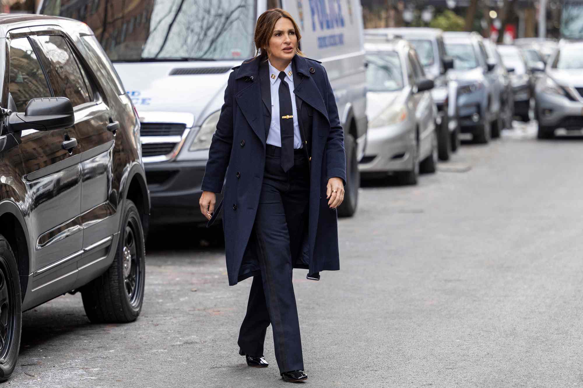 Mariska Hargitay in her iconic blue police uniform from Law & Order: Special Victims Unit, holding a badge with a serious expression