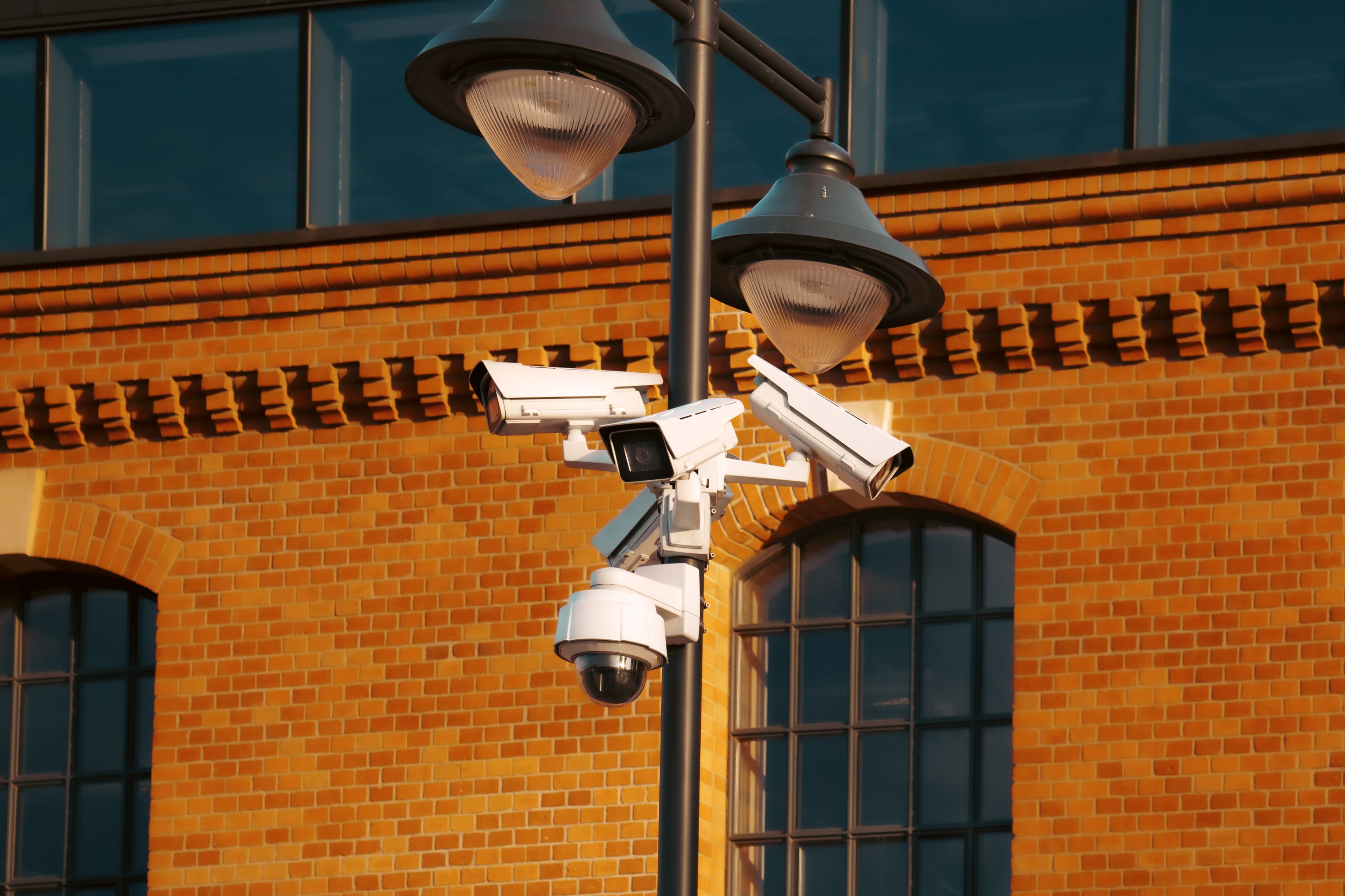 A modern street-mounted security camera with a glowing LED ring, capturing an urban street scene at night under warm sodium lights.