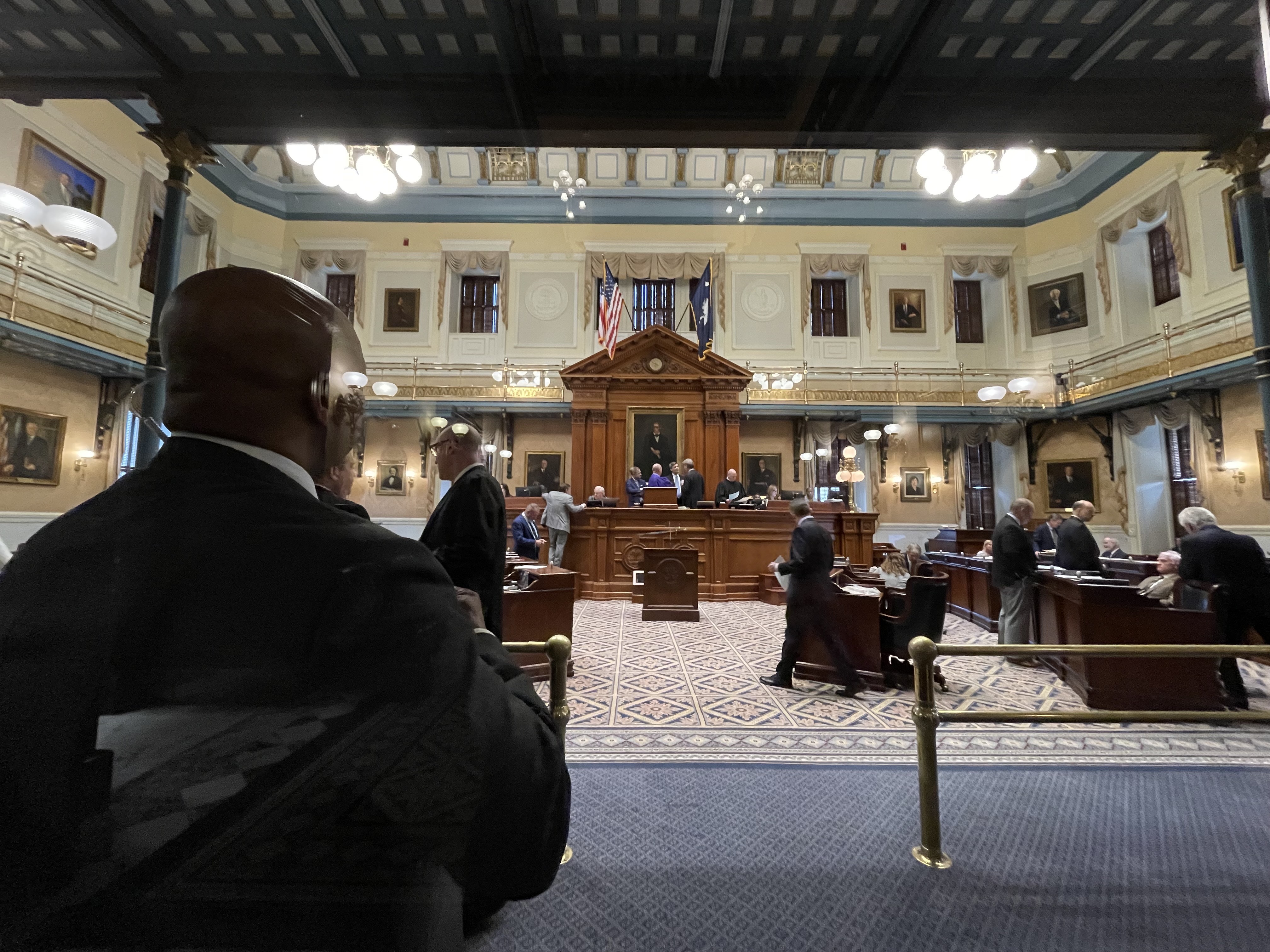 A wooden gavel resting on a desk inside the crowded US Senate chamber with legislators in the background