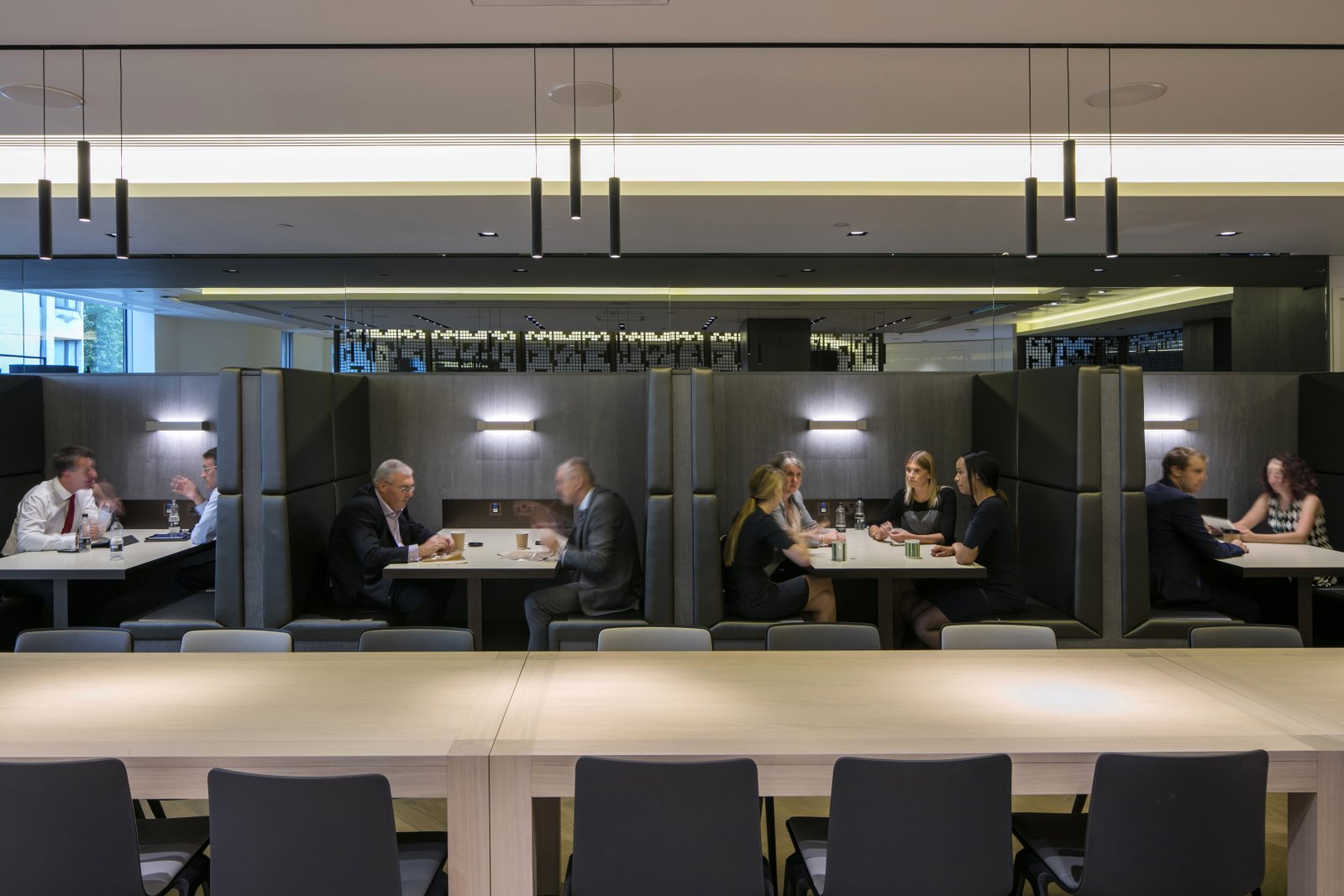 Groupe de professionnels divers en tenue de travail engagés dans une discussion sérieuse autour d'une table de conférence moderne dans un bureau londonien avec vue sur la skyline de la ville