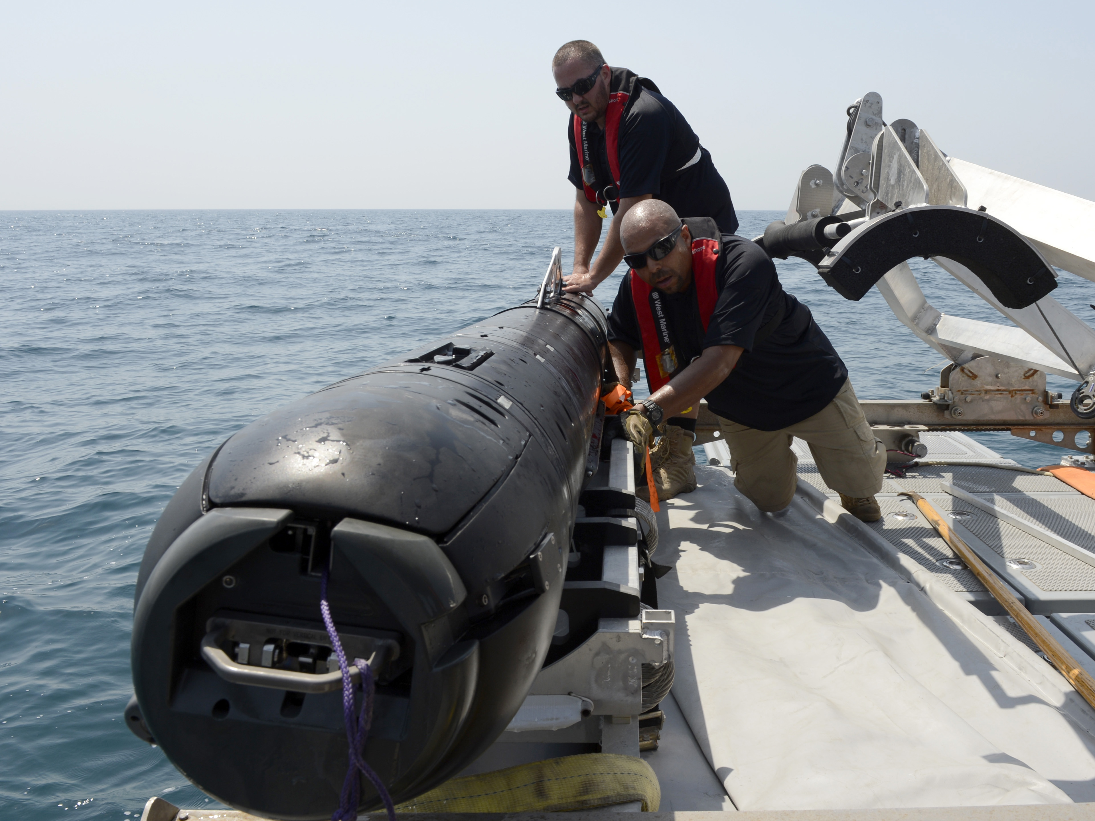 Un technicien inspectant un véhicule sous-marin autonome près de la surface, avec du matériel naval en arrière-plan