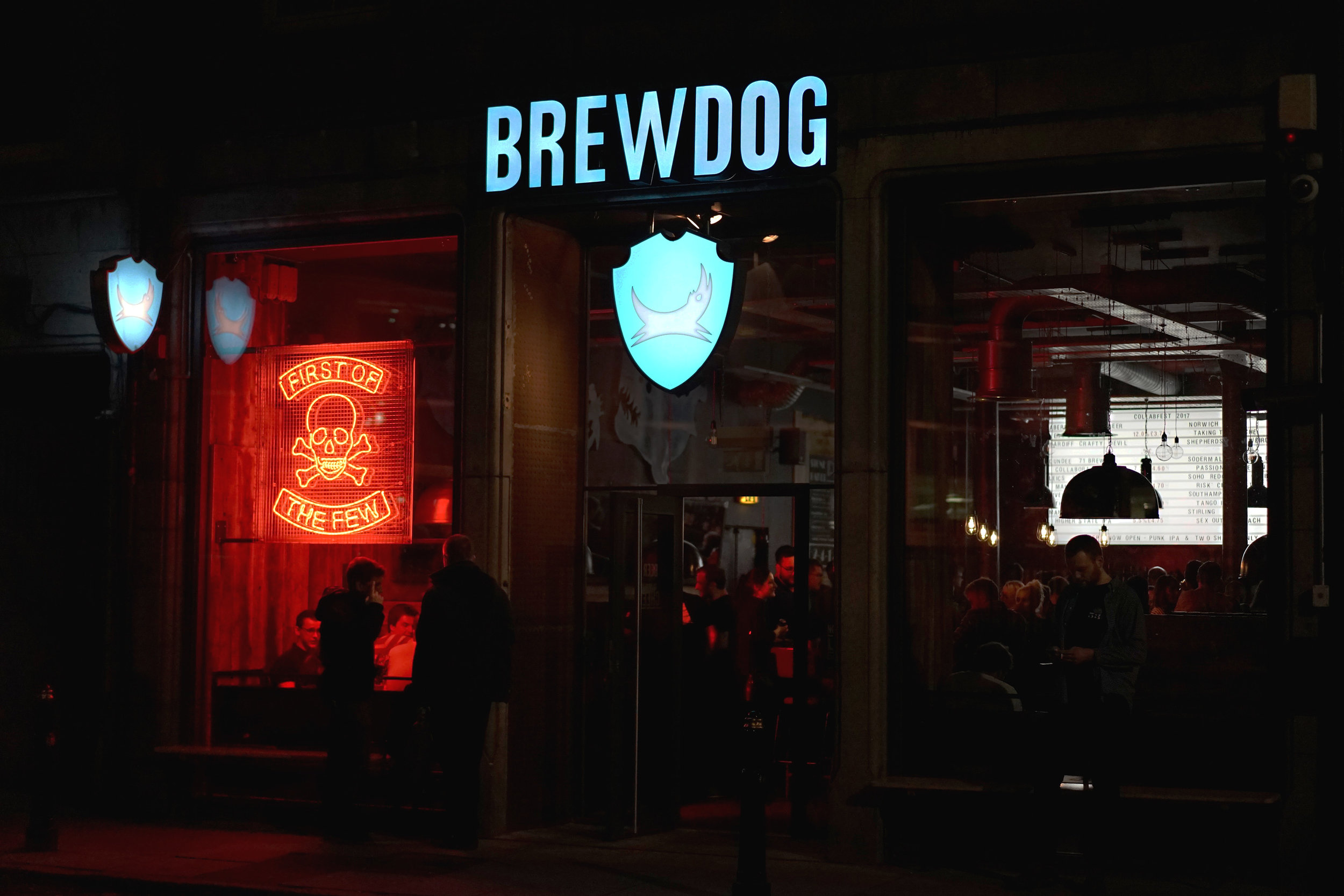 Rows of BrewDog beer taps and branded bottles glowing under a neon sign in a modern British pub setting
