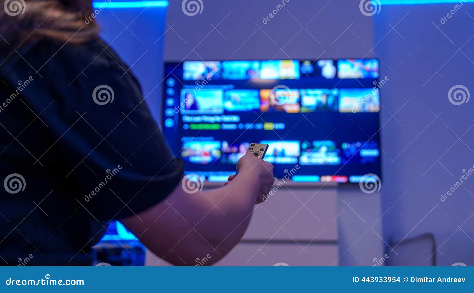 A cozy living room with a large flat-screen TV displaying a modern streaming app interface, a hand holding a sleek remote control in the foreground, and soft ambient lighting.