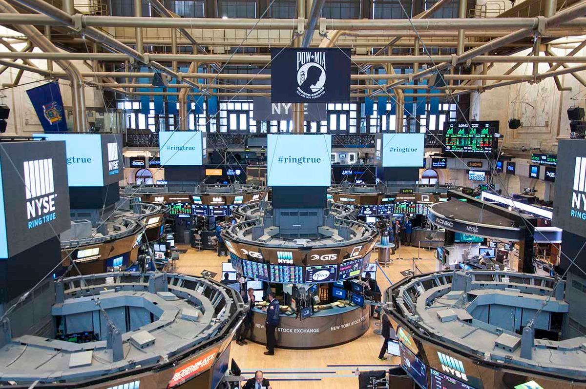 Busy trading floor at the New York Stock Exchange with multiple digital screens displaying financial data and traders in motion