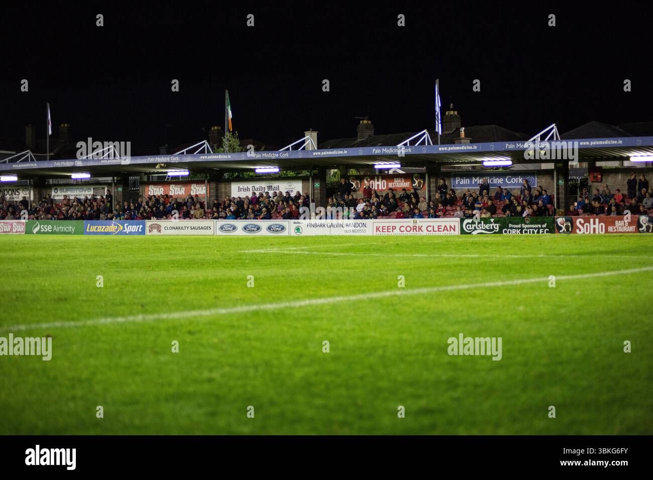 A packed football stadium at night, with fans holding flags and the pitch glowing under floodlights.