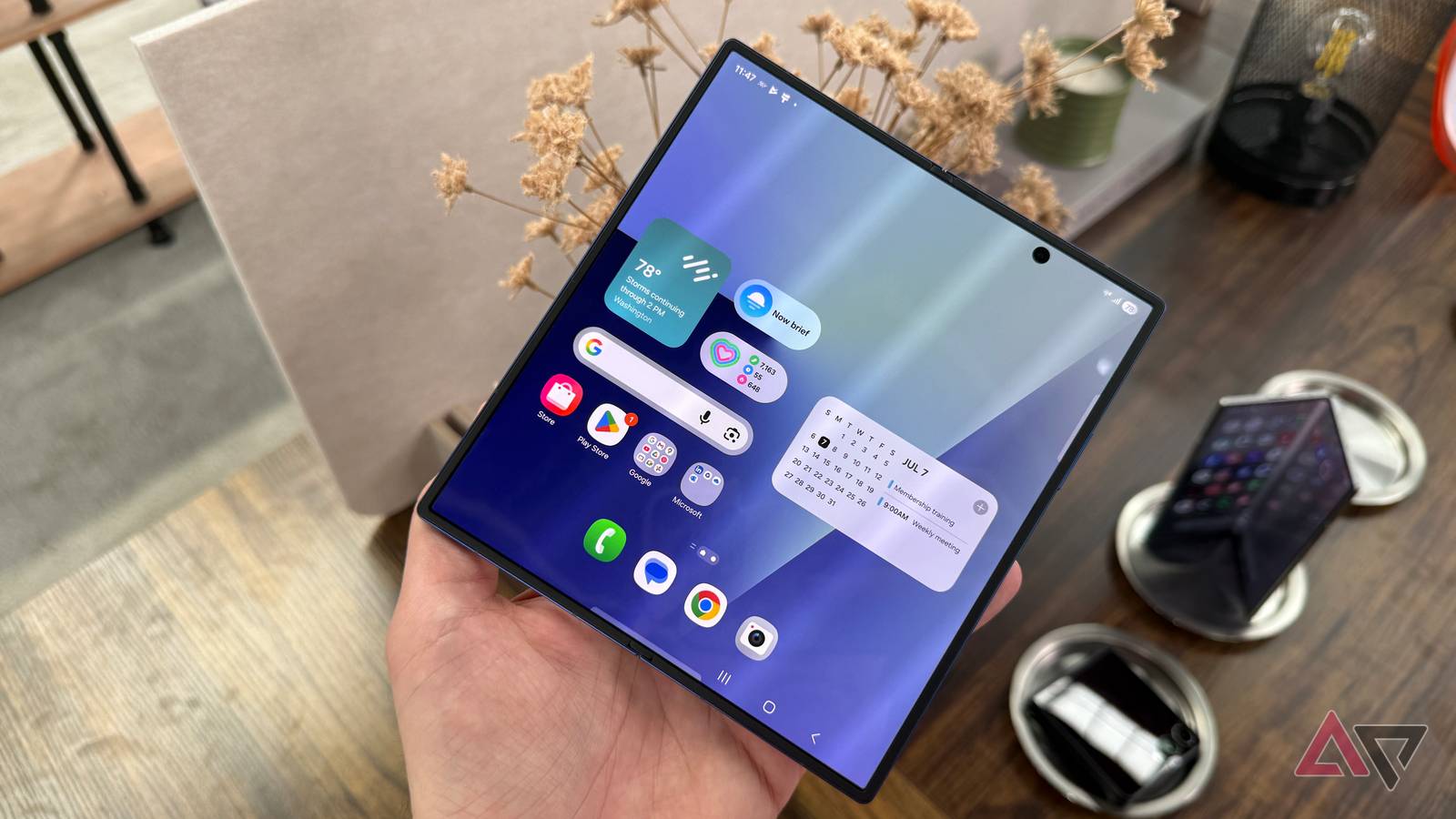 A foldable smartphone with a large unfolded display resting on a wooden desk