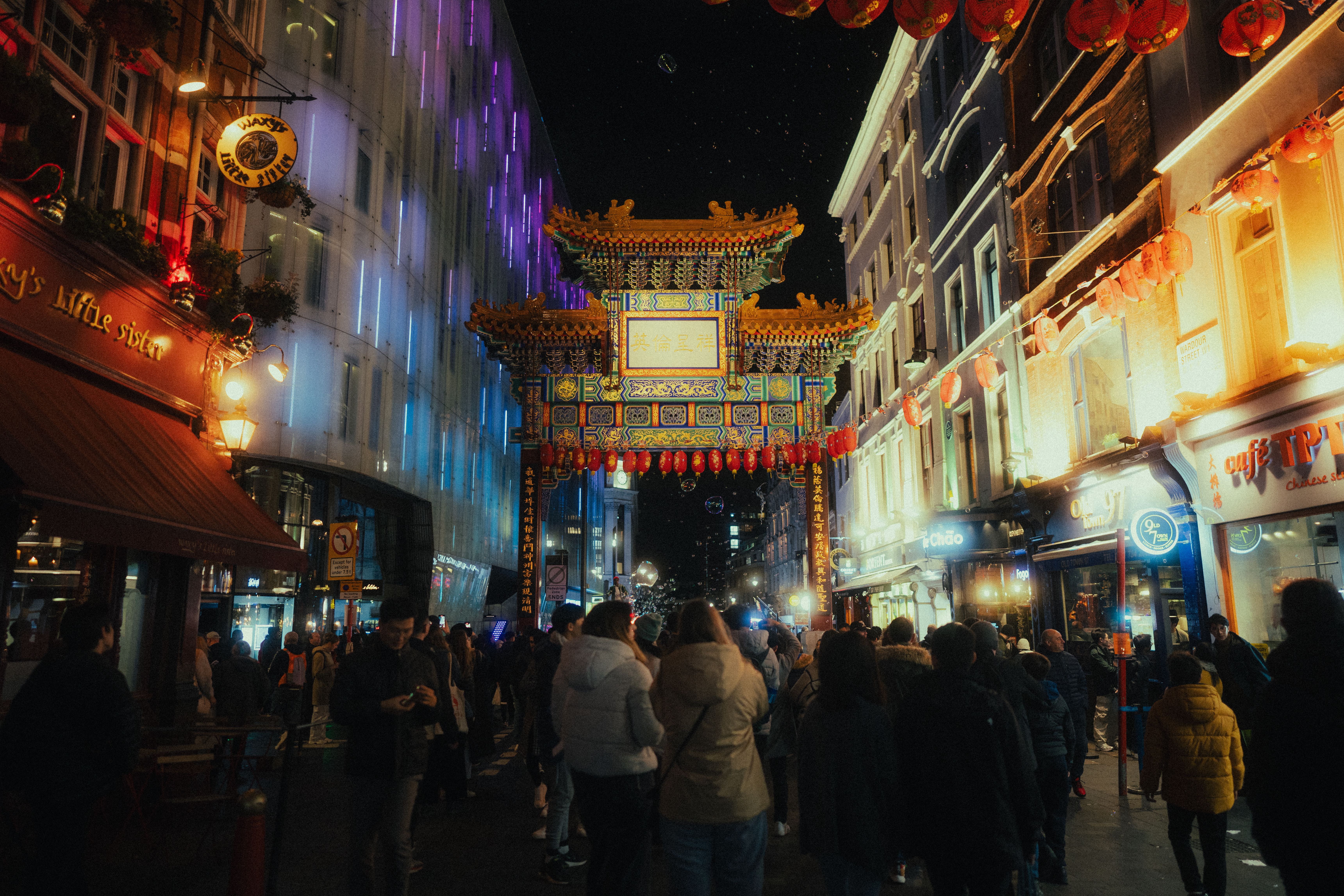 A bustling London street at night with glowing neon signs and a crowd of people walking past a storefront