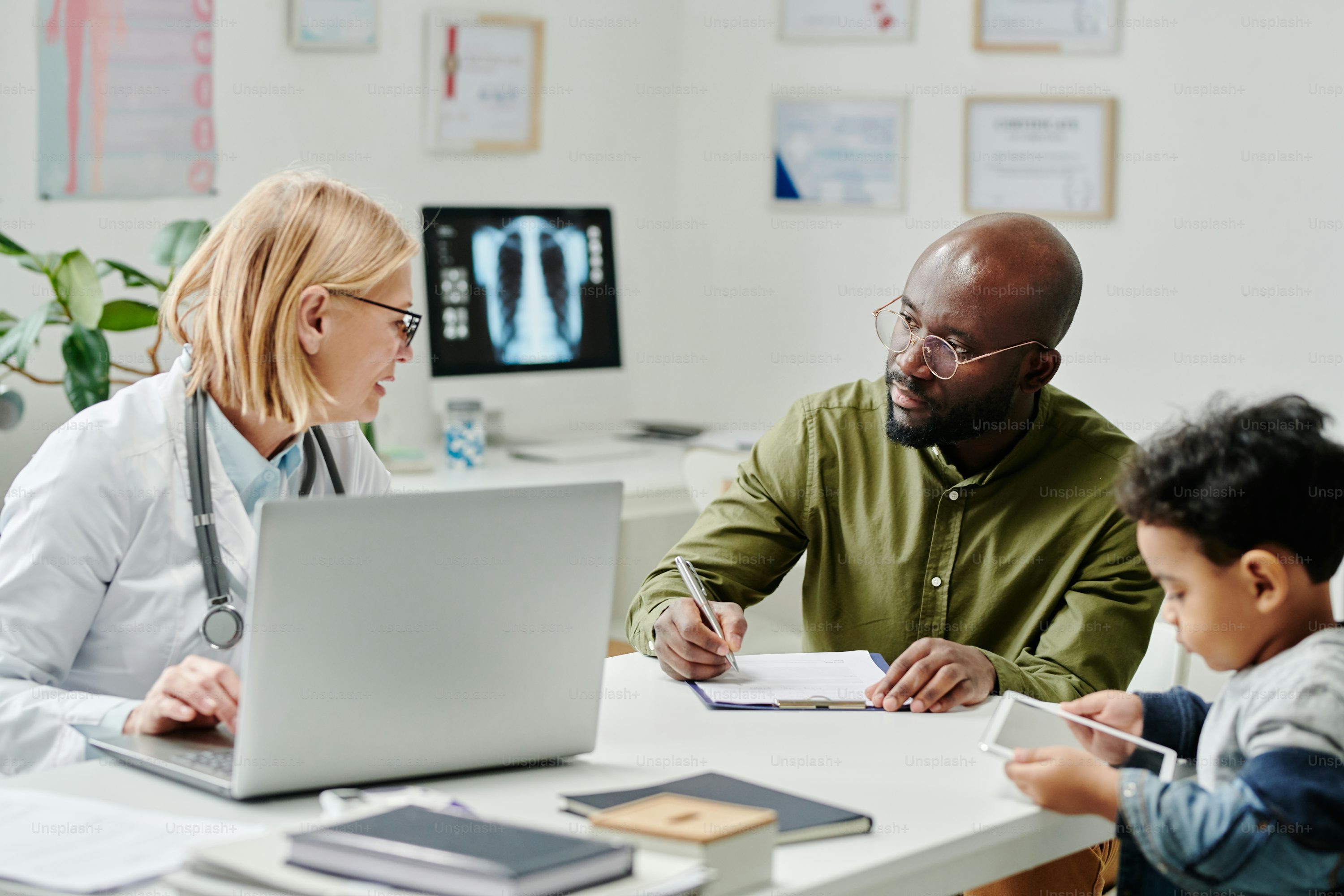 A doctor in a white coat reviewing digital health data on a laptop while speaking with a patient in a modern medical office
