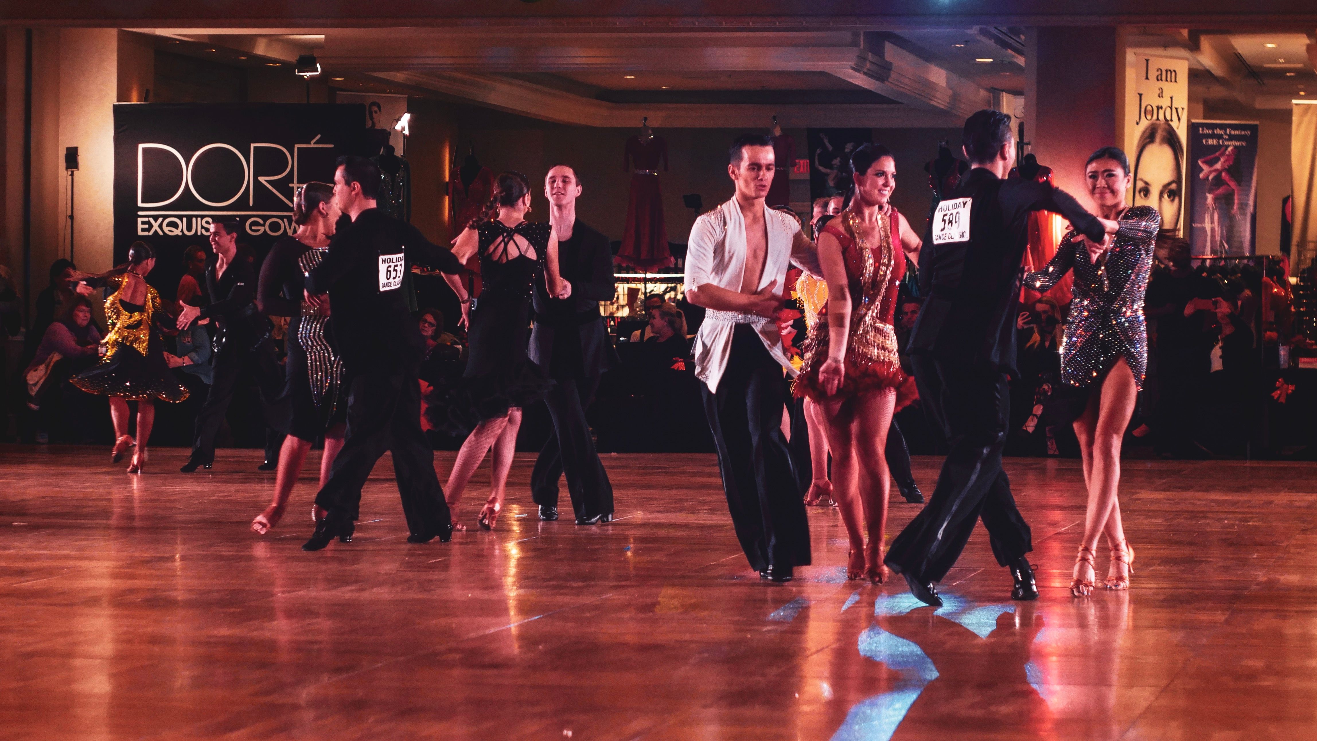 Professional ballroom dancers performing under bright stage lights on a polished wooden floor